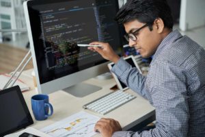 developer comparing code on monitor while looking at sheet of paper